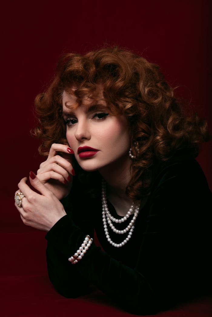 Elegant vintage-style portrait featuring a woman in pearls on a rich maroon backdrop.